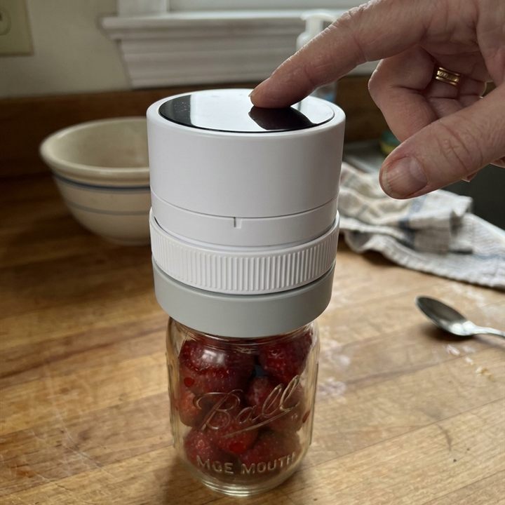 A finger pressing the button on the ROKUME sealer fitted to a jar of strawberries